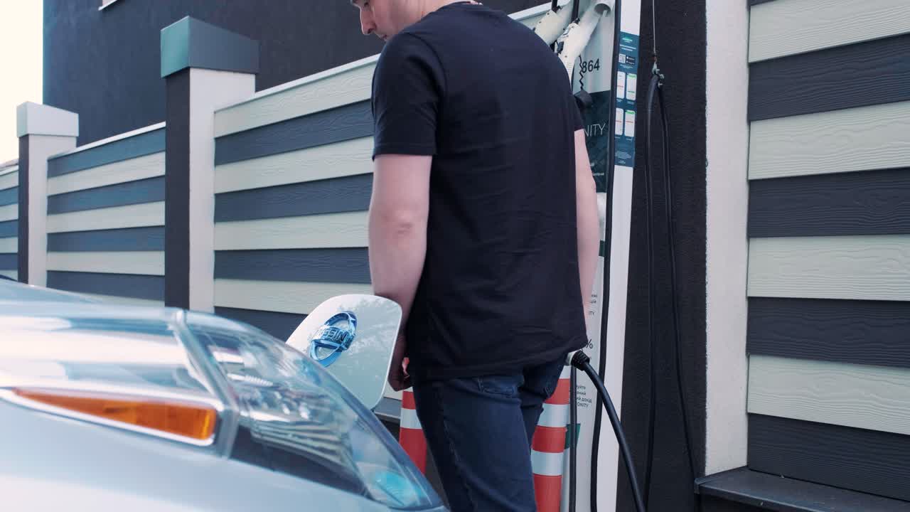 전기 자동차의 연료 충전 과정: 전기 에코 자동차가 충전하는 치 아래의. 전기 자동차 충전 치는 자동으로 열립니다. 남성 손이 발기 된 자동차를 입합니다.