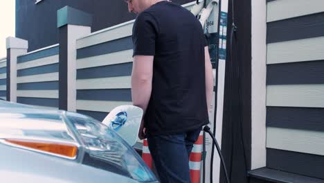 proceso de reabastecimiento de combustible de un automóvil eléctrico. un disparo debajo de la escotilla donde se carga el automóvil ecológico eléctrico. la escotella de carga del automóvil eléctrico se abre automáticamente. una mano masculina inserta un automóvil erecto