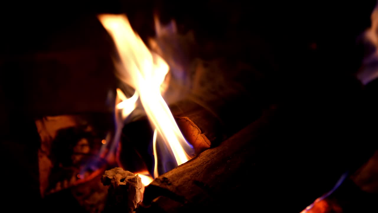 Fire in fireplace. Firewood burning in fireplace for heating at home in winter season. Wooden logs in flame on dark background. Macro shot.