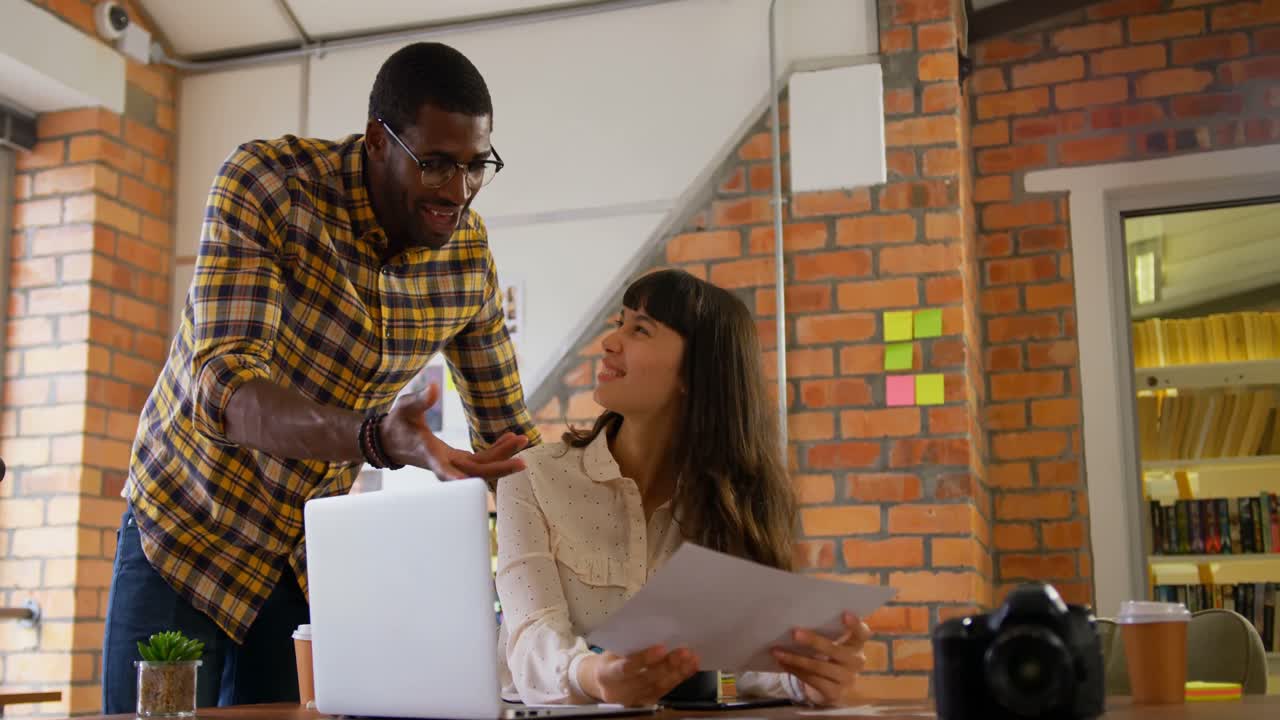 Graphic designers discussing over photograph at desk in modern office 4k