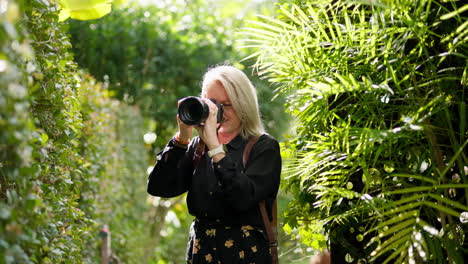 blonde professional wedding photographer candid shooting outdoors in green bush garden, 4k slow motion