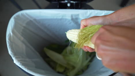 close up of woman husking sweet corn and throwing waste in garbage