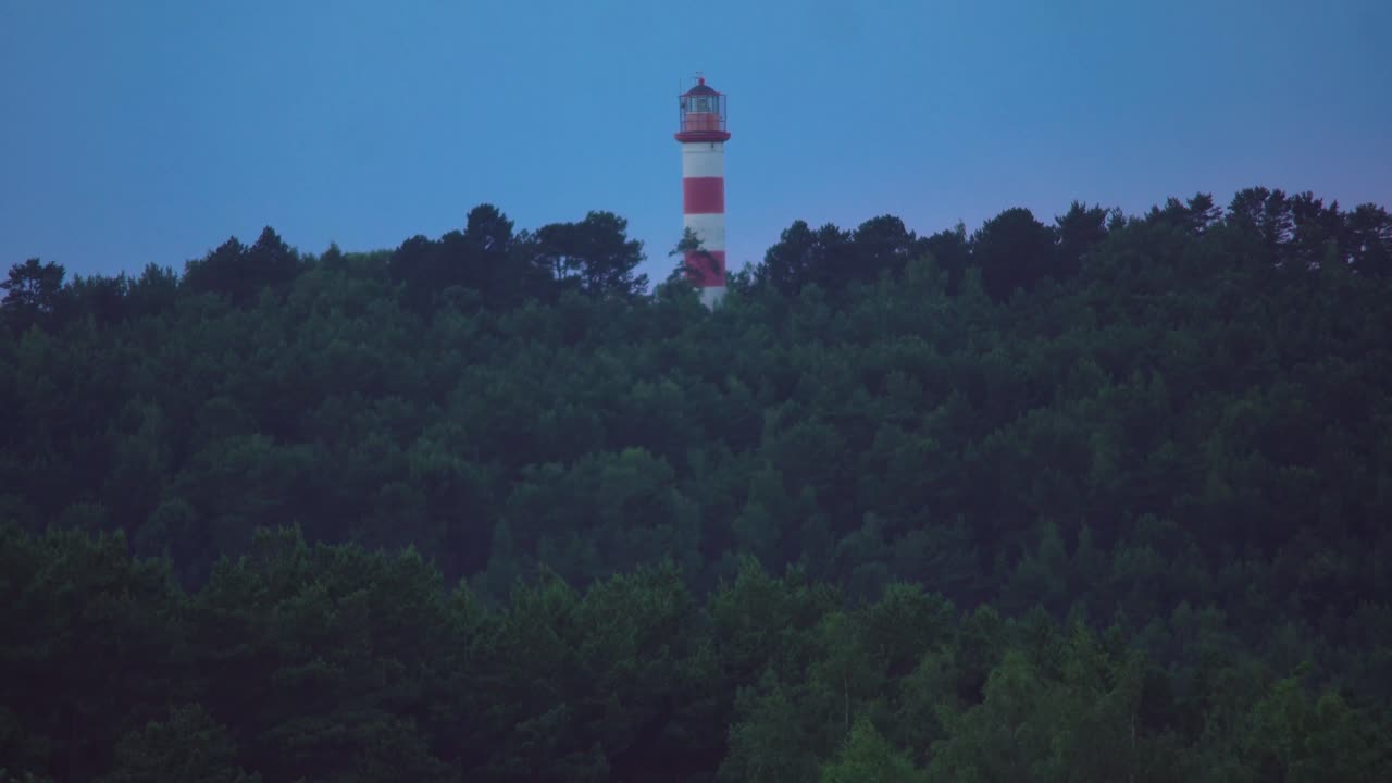 Tilting shot of forest which leads to abandoned lighthouse on the top of the hill