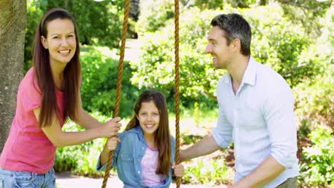 padres empujando a su hija en un columpio en el parque