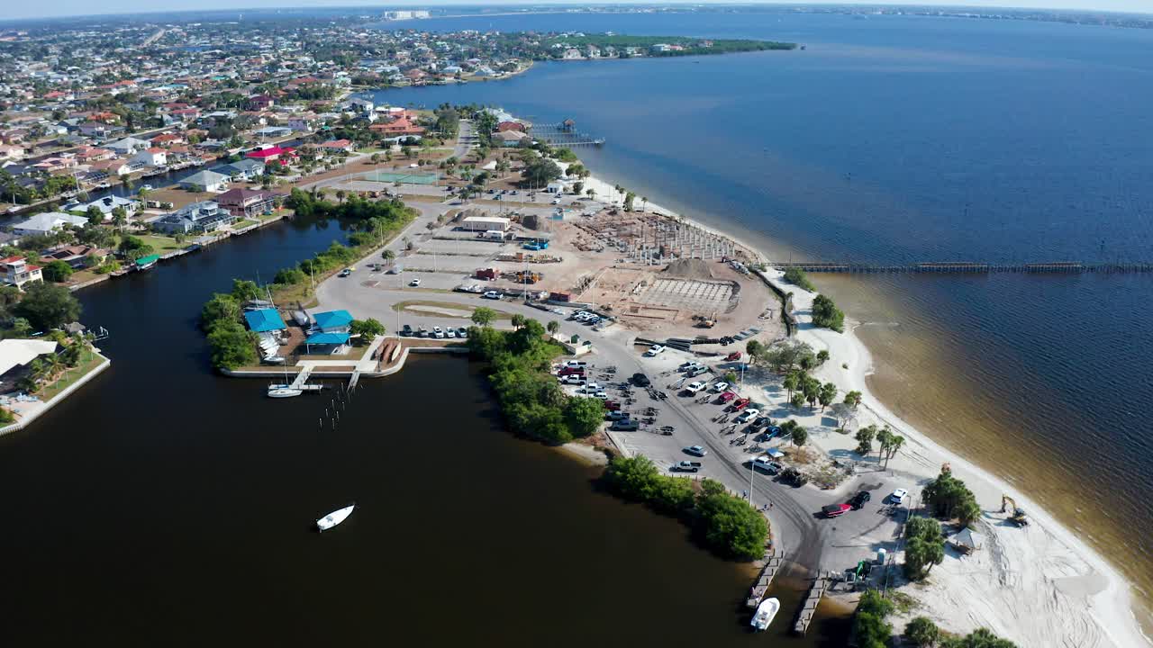 Rannikkoalueen rakennustyömaa, jossa on perustus- ja paalutustöitä sekä rakennusmateriaaleja. Alueen ympärillä on pysäköintialueita, satama-altaita ja hiekkarantaa aurinkoisessa Floridassa lähellä tyyniä vesiä.