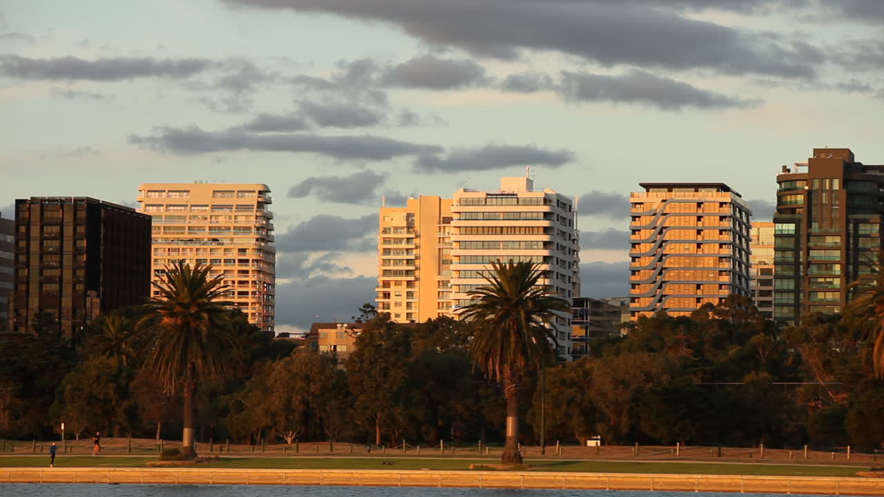Runners jogging along Albert Park Lake, Melbourne, Australia. Traffic moving along famous inner city drive while sun sets over the building below.