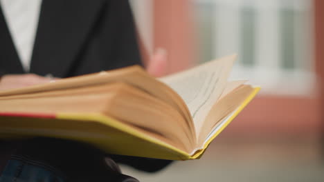 close-up of book pages being turned by a woman with well-manicured nails and adorned with a ring, subtle blurred background enhancing focus on the text