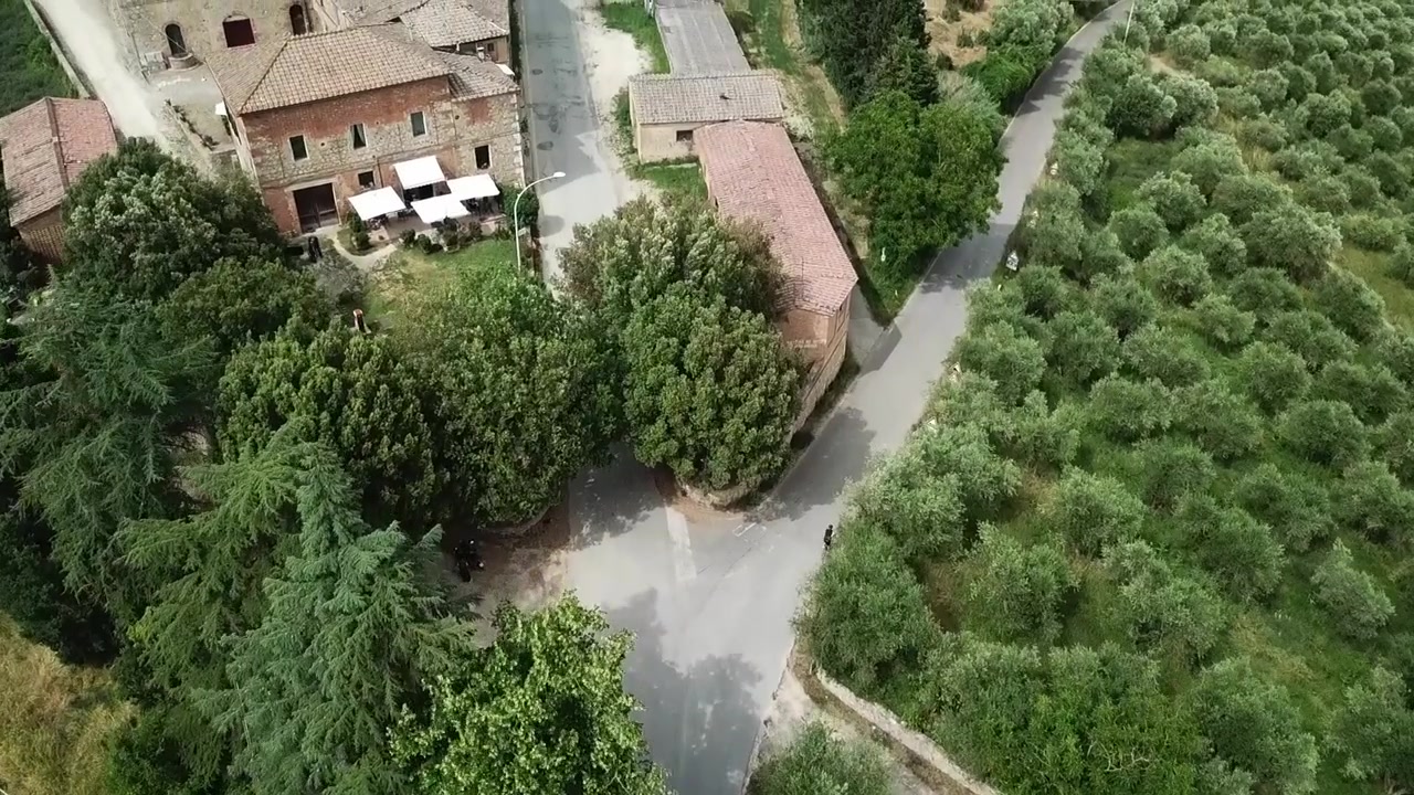 Vista aerea di un villaggio toscano rustico con edifici storici in pietra, strada tortuosa e rigogliosa vegetazione mediterranea in Toscana, Italia