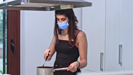 young woman cooking food for delivery in protective mask