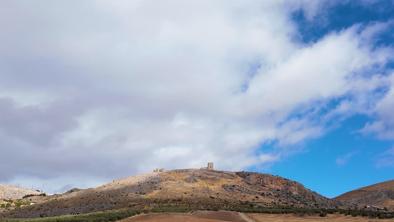 Timelapse aereo statico del castello Castillo de la Estrella a Teba, Spagna, che mostra ombre di nuvole in movimento sulla collina e sulla fortezza sotto un cielo blu.