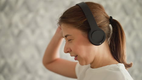 lady shields eyes with headphones while jogging indoors. athletic woman enjoys earpieces while training on treadmill in gym. fun during exercising