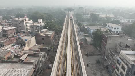 Aerial-drone-backward-moving-shot-over-a-metro-train-passing-on-an-Orange-Metro-Rail-track-near-McLeod-Road-Lahore,-Pakistan-at-daytime