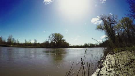 early spring riverside timelapse of two levels of clouds on sunny day with trees and branches at riverside