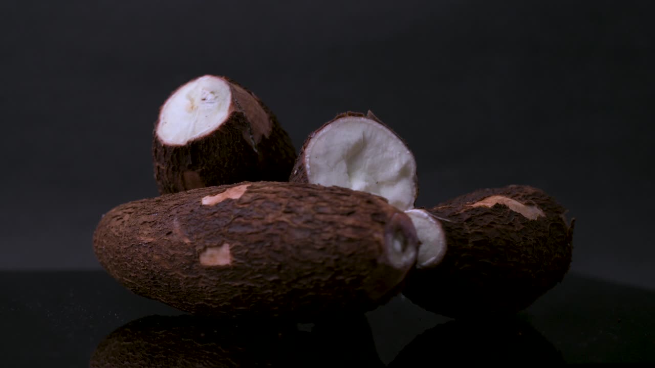 4K rotating wide shot of fresh cassava root (yuca, manioc) with rough brown skin and white starchy interior. Perfect for tropical cuisine, exotic food, gluten-free cooking, and nutrition