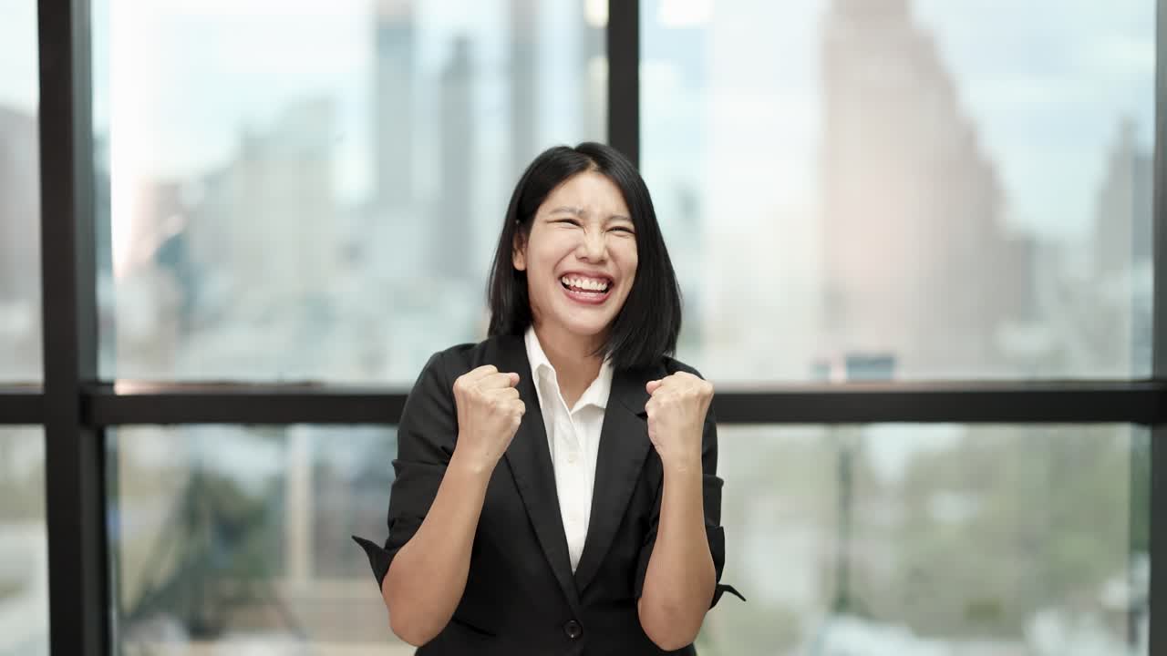 Asian businesswoman in suit celebrates achievement, joyful expressions, natural light, static camera, office background
