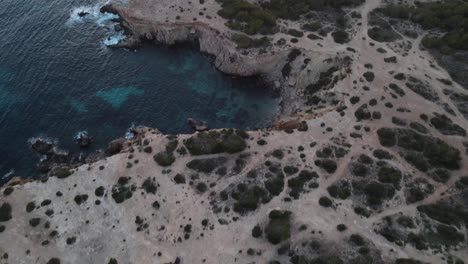 Toma-Aérea-De-Un-Dron-De-Un-Monumento-Prehistórico-En-Ibiza-Que-Termina-En-Una-Increíble-Puesta-De-Sol-Fusionándose-Con-Una-Isla-En-El-Fondo-Del-Mar.