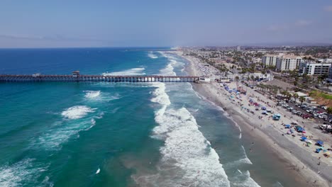 Drohne,-Die-über-Den-Strand-Am-Meer-In-Richtung-Pier-Und-Strandresorts-Fliegt