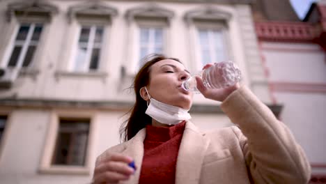 Schönes-Mädchen-Mit-Medizinischer-Schutzmaske-Und-Modischer-Kleidung-Trinkt-Wasser-Mit-Flasche