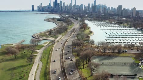 Aerial-reveal-of-Chicago-Downtown,-US-Highway-41,-empty-Diversey-Harbor-and-Lakefront-trail-on-sunny-autumn-day-with-midday-traffic