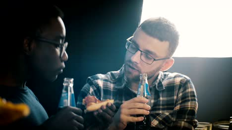grupo multiétnico de amigos comiendo pizza y tomando bebidas en una fiesta de casa. los jóvenes disfrutan de la comida en la mesa de la cocina