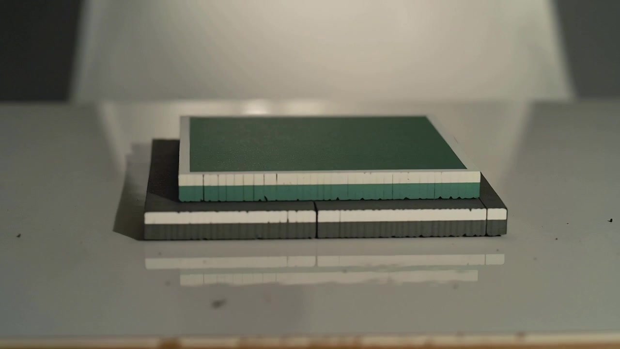Orbiting camera revealing stacked square block on glossy white tabletop, revealing layered profile