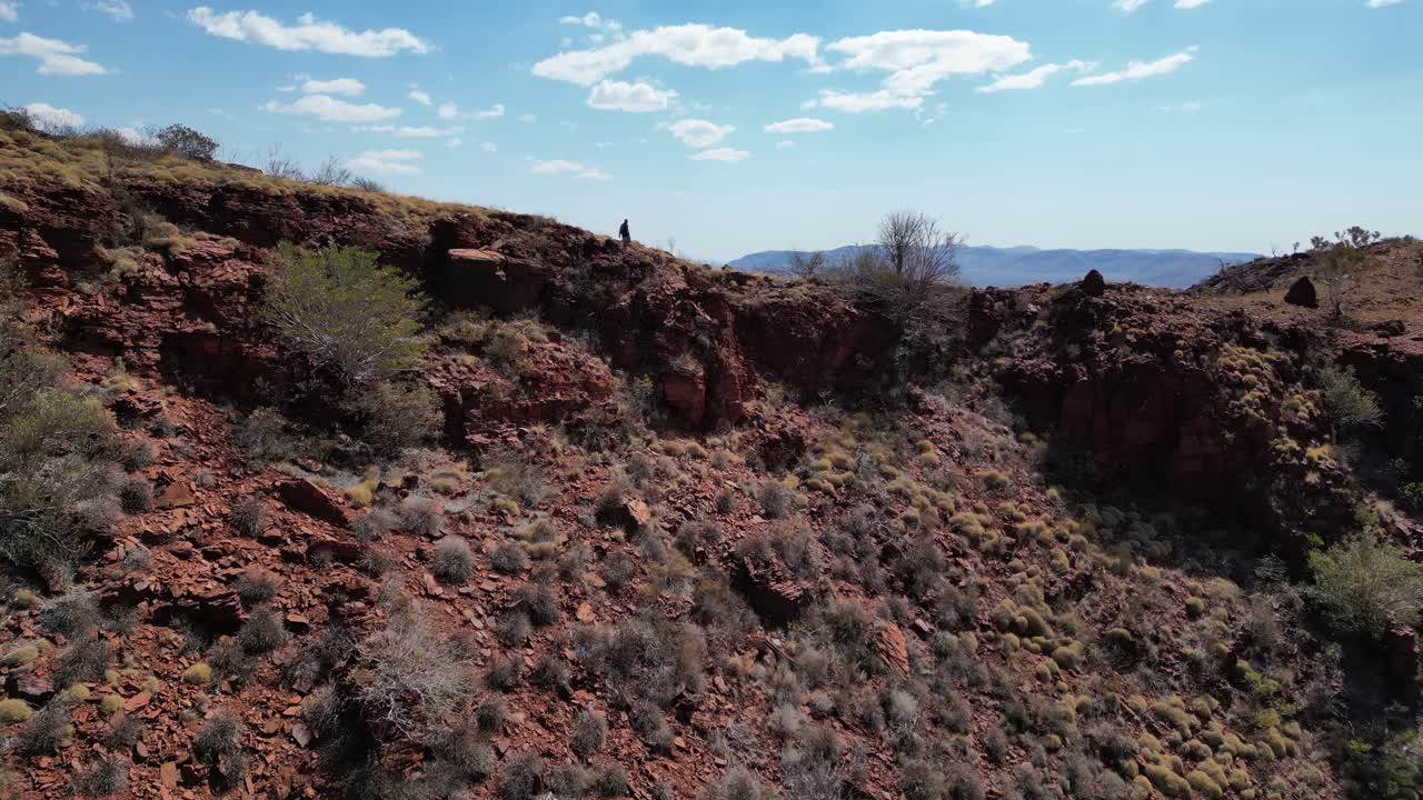 vuelo de avión no tripulado en cámara lenta que muestra a un excursionista caminando entre las montañas en el desierto australiano durante un día soleado