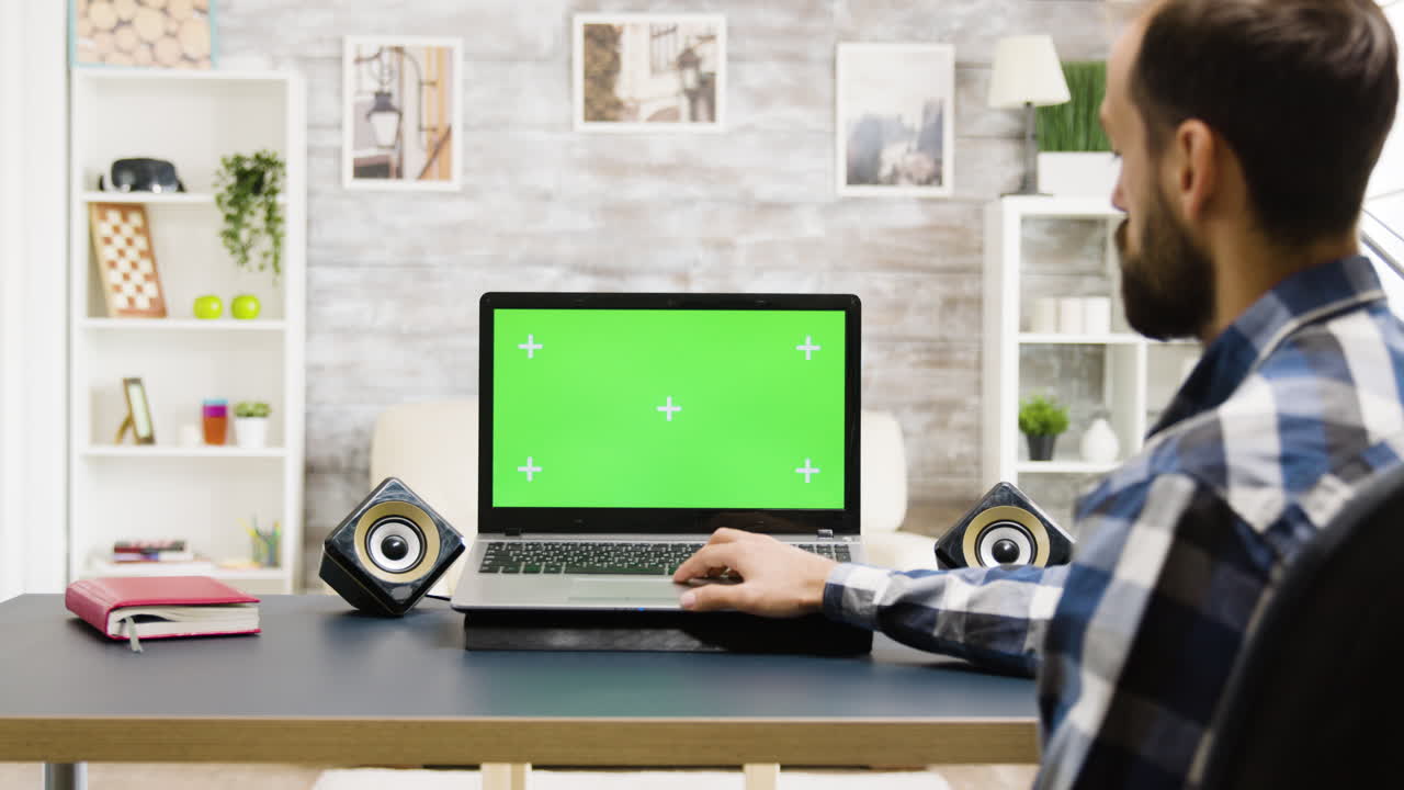 Man working on laptop with green screen at home
