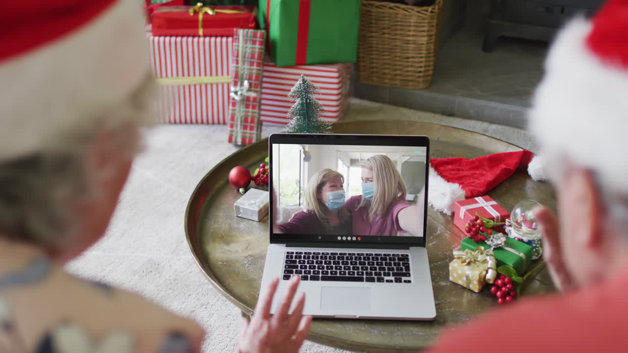 una pareja de ancianos caucásicos usando una computadora portátil para una videoconferencia de navidad con la familia en la pantalla