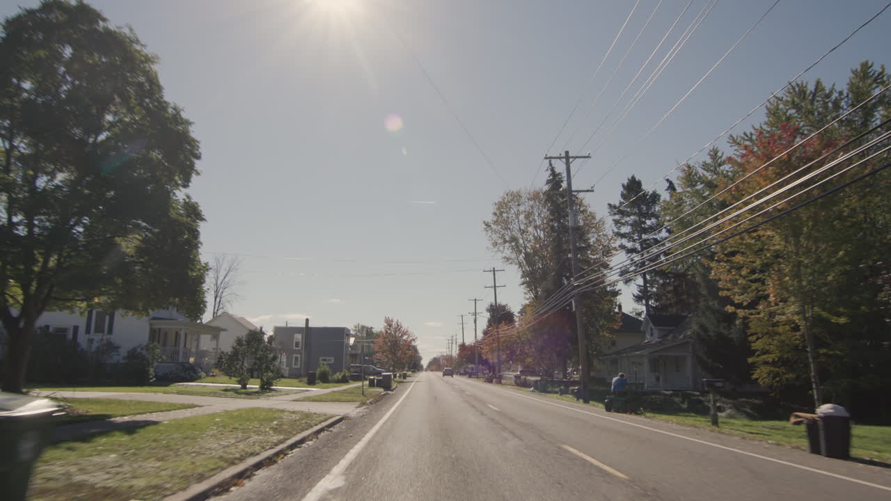 un coche conduciendo por una acogedora calle estrecha de una típica ciudad estadounidense. el sol brilla a través de los árboles. otoño, hora de halloween