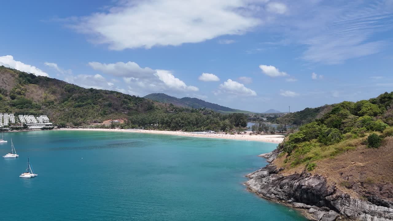 드론 영상은 푸켓의 해안선의 조용한 비행을 포착합니다. 푸켓의 바물, 울창한 초록색, 그리고 은 하늘 아래 정박한 요트들을 보여줍니다.