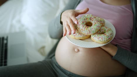 Top-view-video-of-cheerful-pregnant-woman-eating-donuts.