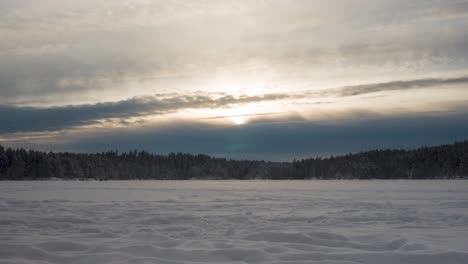 distant view of people walking on frozen lake with dense forest during sunset