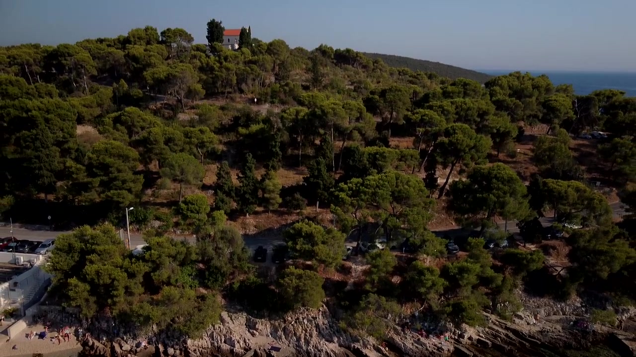 Maslinica, Croazia, la costa rocciosa incontra le limpide acque turchesi dell'Adriatico, ripresa aerea che si allontana da persone che giocano in acque scintillanti.