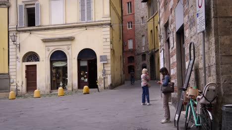 two women stand in a quiet, historic tuscan street with colorful buildings and a peaceful vibe