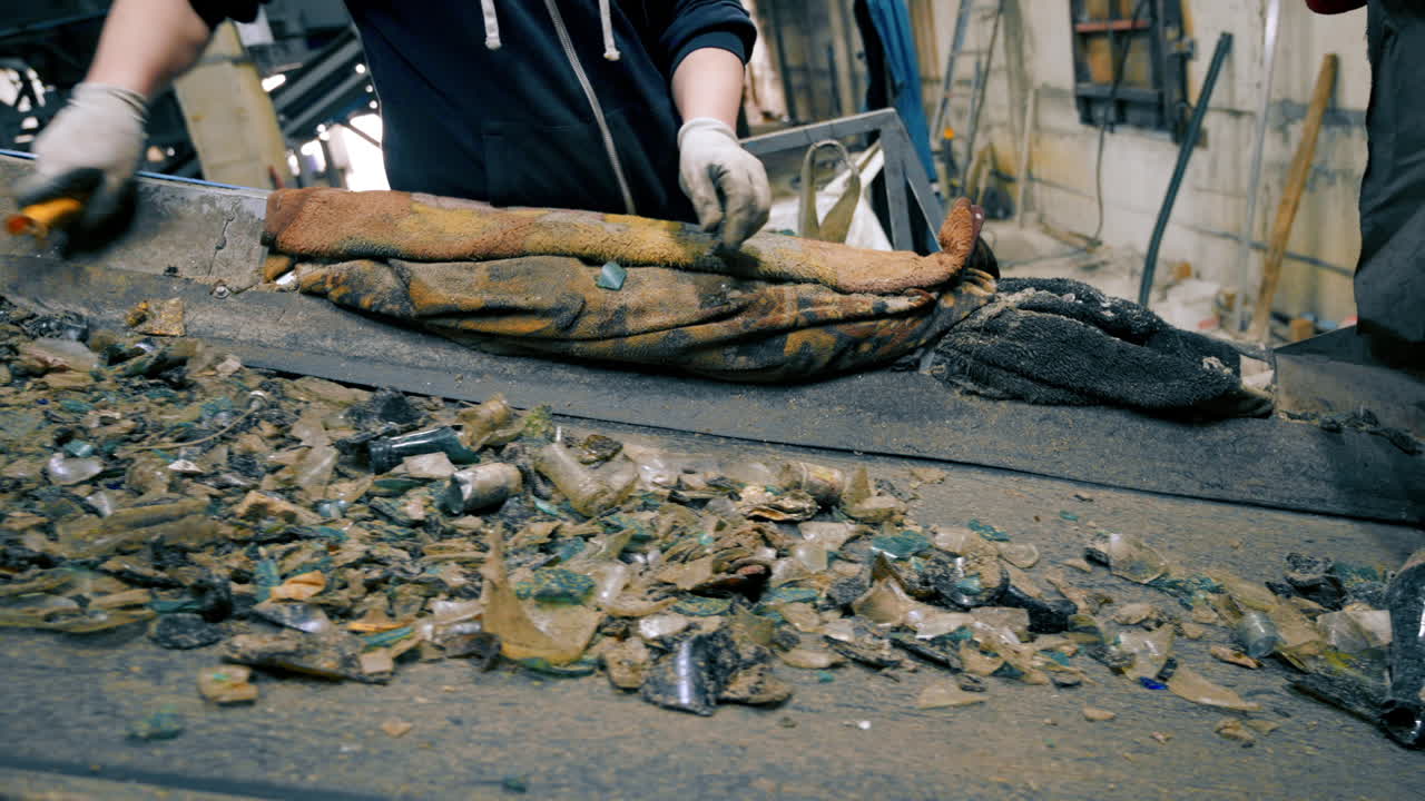 Worker in special gloves sorting glass garbage on a conveyor belt at waste sorting plant