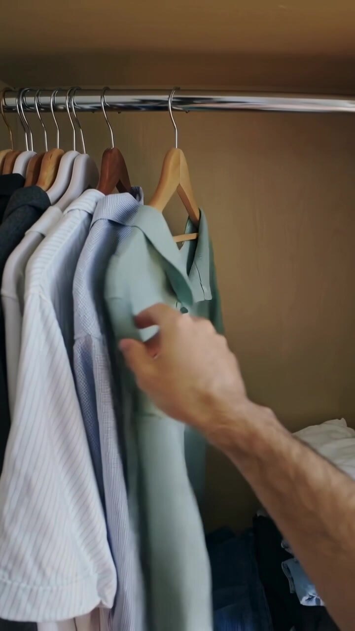 Video verticale: Avambraccio nudo che si allunga ispezionando una camicia verde su una gruccia nell'armadio, controllando l'etichetta