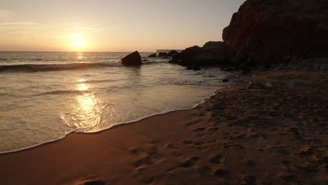 golden light reflects on gentle waves at a rocky beach in algarve, portugal, during a peaceful sunset