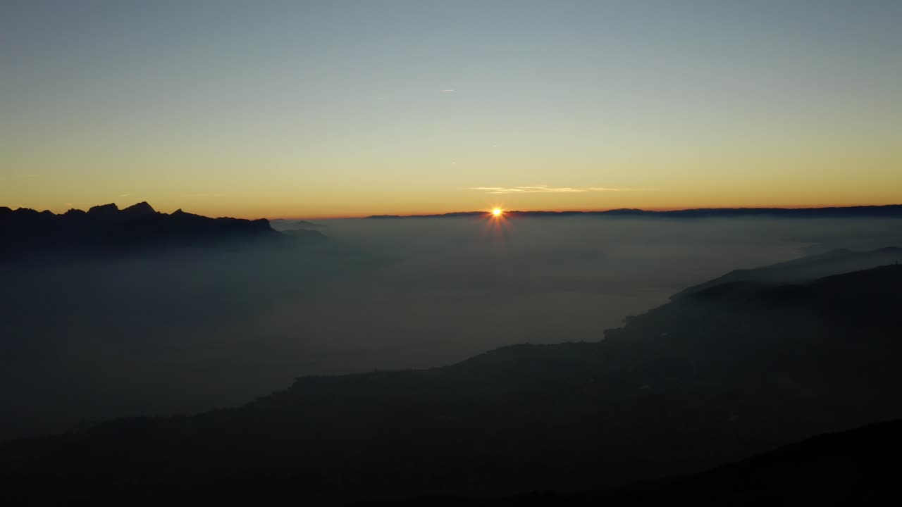 sol desapareciendo por debajo del horizonte sobre el mar de niebla niebla que cubre el lago léman - suiza