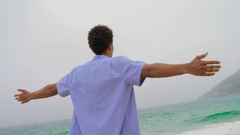 Rear-view-of-African-American-man-standing-with-arms-outstretched-on-the-beach-4k