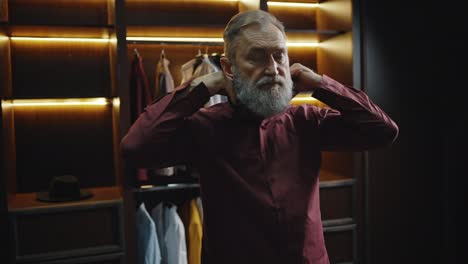 stylish bearded mature man getting ready in morning, buttoning up his shirt in dressing room, empty space
