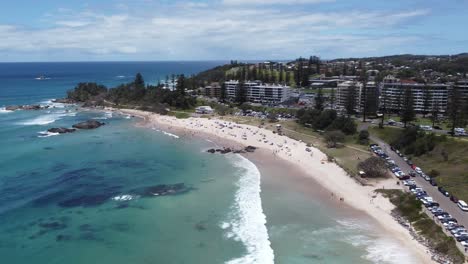 Vista-Aérea-De-Una-Hermosa-Playa-De-Arena-Con-Un-Pueblo-Costero-Al-Fondo