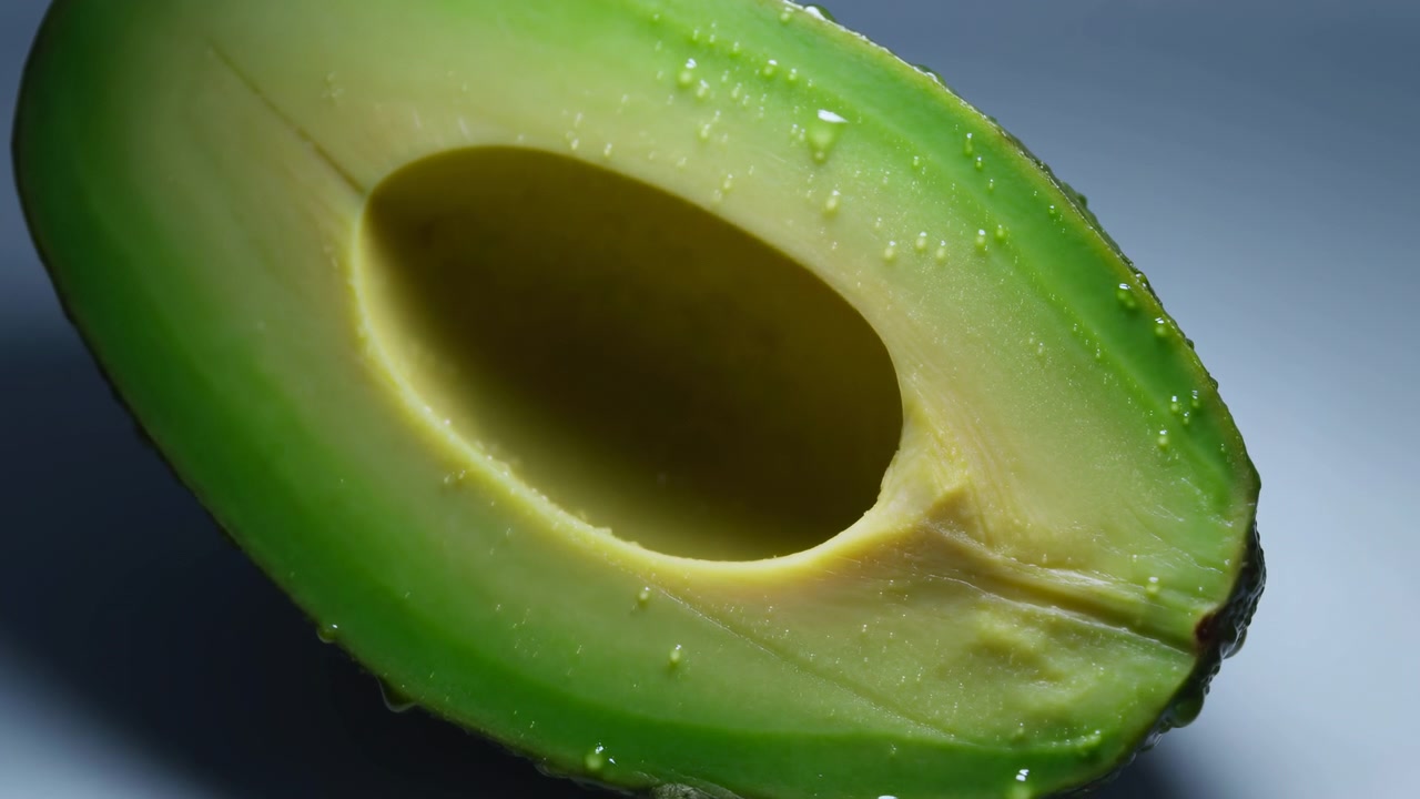Avocado tagliato a metà esposto su uno sfondo neutro con illuminazione soffusa, creando una prospettiva pulita e fresca. Questa vista ravvicinata evidenzia la polpa e la buccia dell'avocado, sottolineandone la
