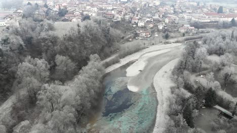drone flies above clear river revealing tolmin town in slovenia on winter morning