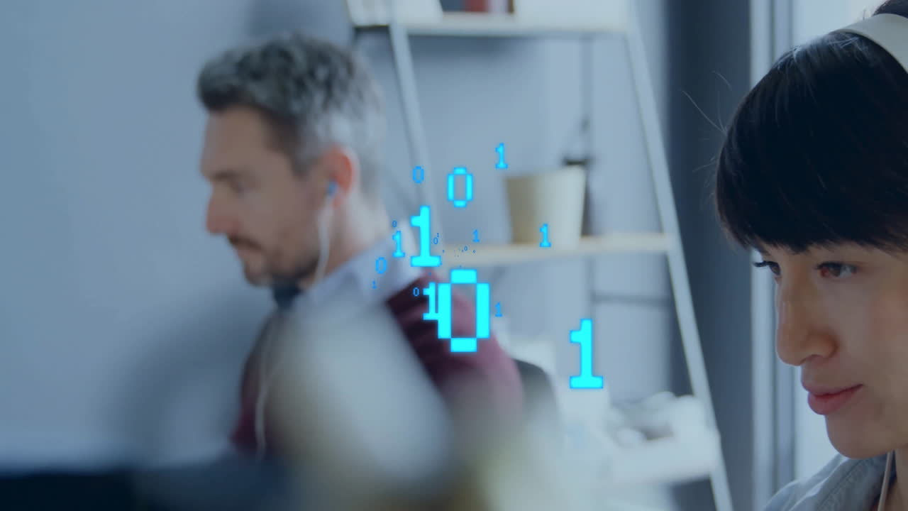Co-workers wearing earphones typing at desks in tech office, displaying floating blue binary digits