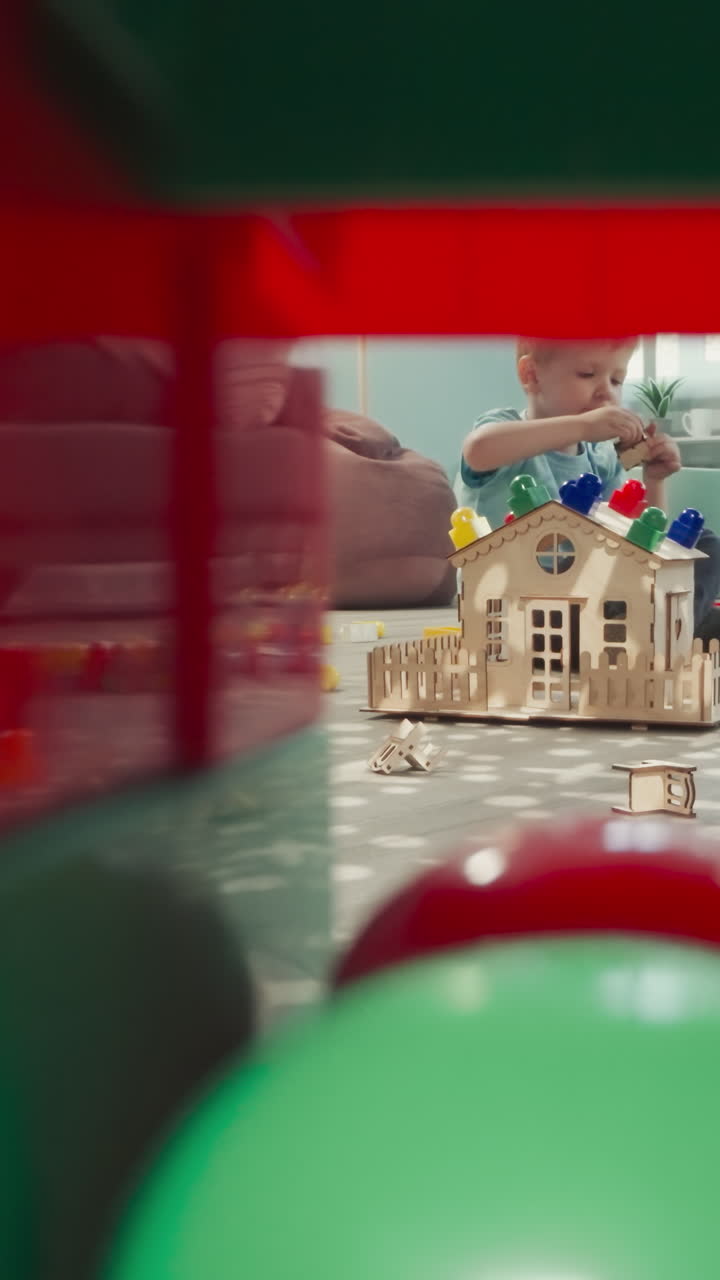 유치원 소녀가 아기 인형을 돌보는 동안 유아가 집을 짓고, 형제 자매가 집에서 장난감으로 놀고, 큐브의 건설에서 클리어링을 통해 볼 수 있습니다.
