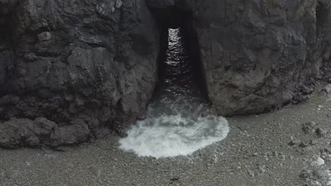 tunnel in rocky shore islet allows grey ocean waves to surge through