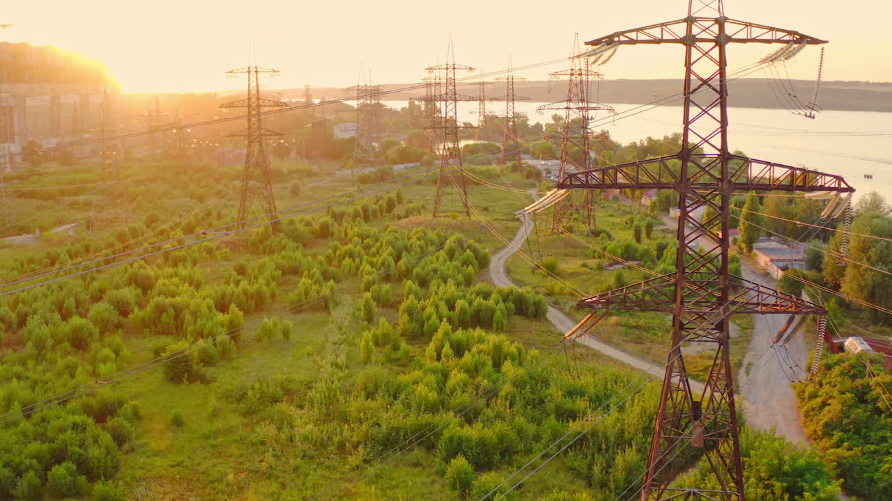Transmission lines in the morning. High voltage electric lines near the river in summer. Tall electric towers at sunset. Aerial view. Slow motion.