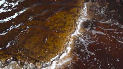 vibrant top down down slow motion footage of clear and cold river water flowing on limestone rocky flat bottom with water waves, foam, bubbles and splashing. the water is reflective and brown colored.