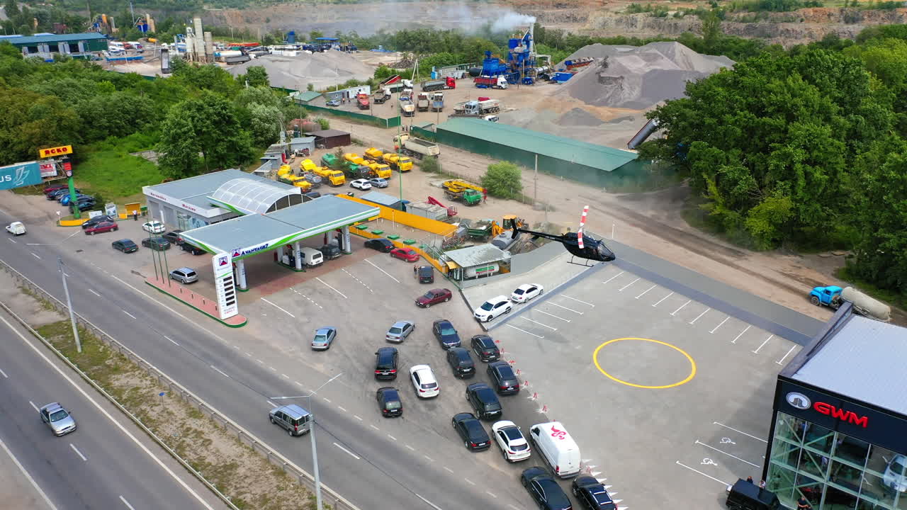 Helipad near the car dealership building. Helicopter landing near the car line to the gas station. Construction site at backdrop. Aerial view.