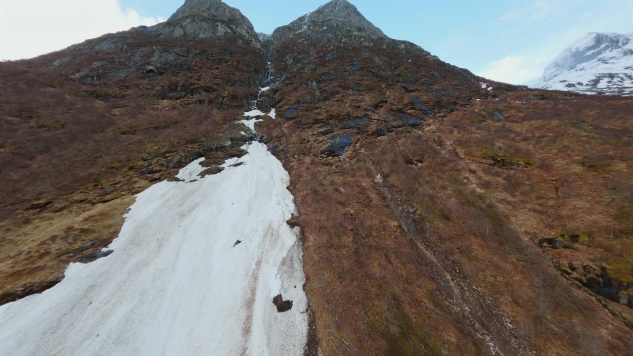Forward push toward a snow-covered mountain ridge with small waterfall in a Norwegian alpine valley.